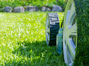 Close-up of a lawn mower cutting grass in a garden, with fresh green grass and blurred stones in the background.