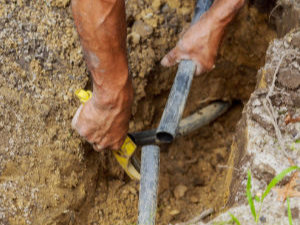 Close-up of a person’s hands repairing or installing a black pipe in a narrow trench in the ground.