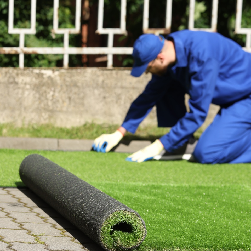 Young man in uniform installing artificial turf outdoors, selective focus